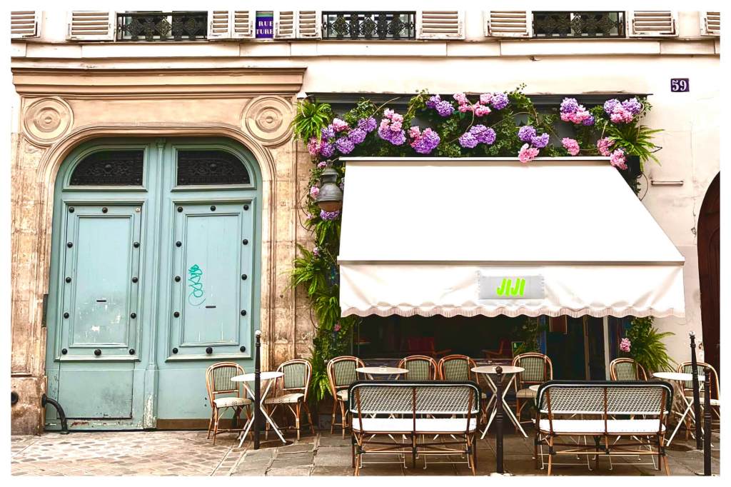 a cafe front at le marais. there is a blue coloured door visible. the cafe has cane chairs and the entrance is decorated by bright coloured hydrangeas.